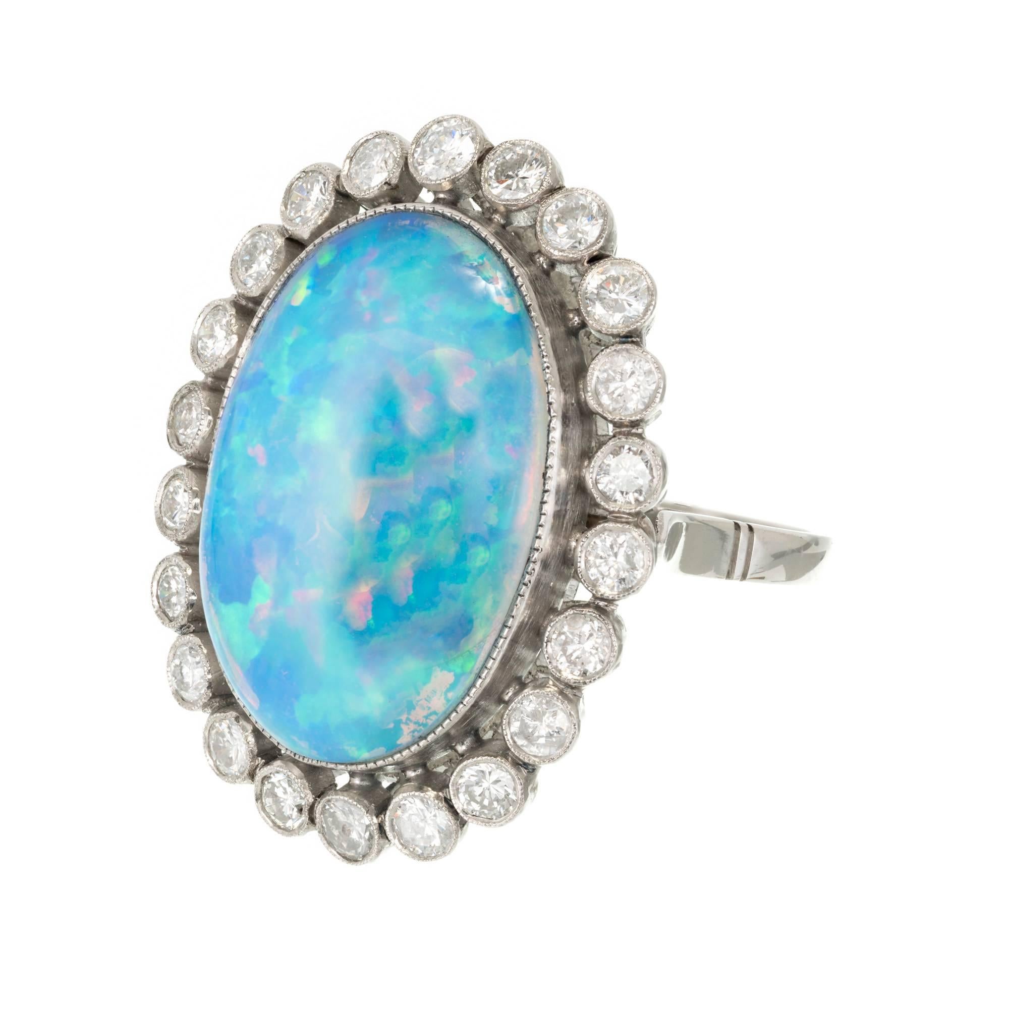 Mid-century Opal ring in handmade Platinum surrounded by bright white shiny transitional cut Diamonds in a halo. Bright blue with distinct red and green flash. 

1 oval cabochon blue with red, orange and green flash Opal, approx. total weight