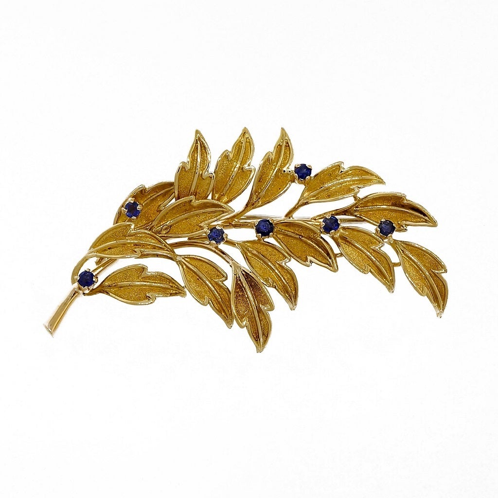Tiffany & Co hand textured 3 dimensional leaf pin made in Italy in solid 18k gold with fine deep blue Sapphires.

7 round blue Sapphires, .05ct each, approx. total weight .35cts
18k yellow gold
Tested and stamped: 18k
Hallmark: Tiffany & Co 18k