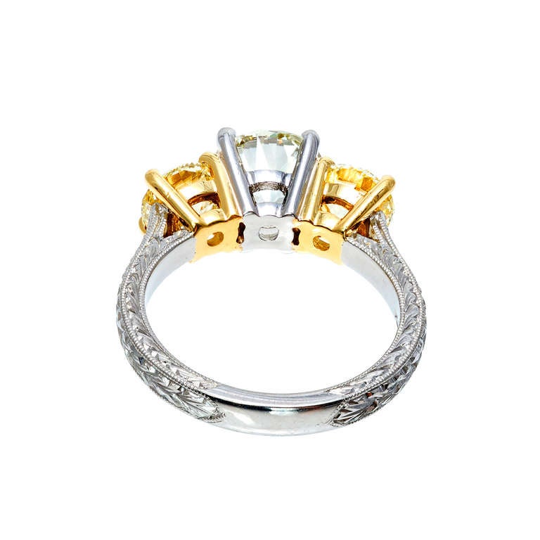 Three stone white and yellow diamond engagement ring. Round center diamond with two yellow diamond accent stones in an engraved Platinum shank and 18k yellow gold under each side diamond.  Raised crowns and small tables.  EGL certified. Crafted in