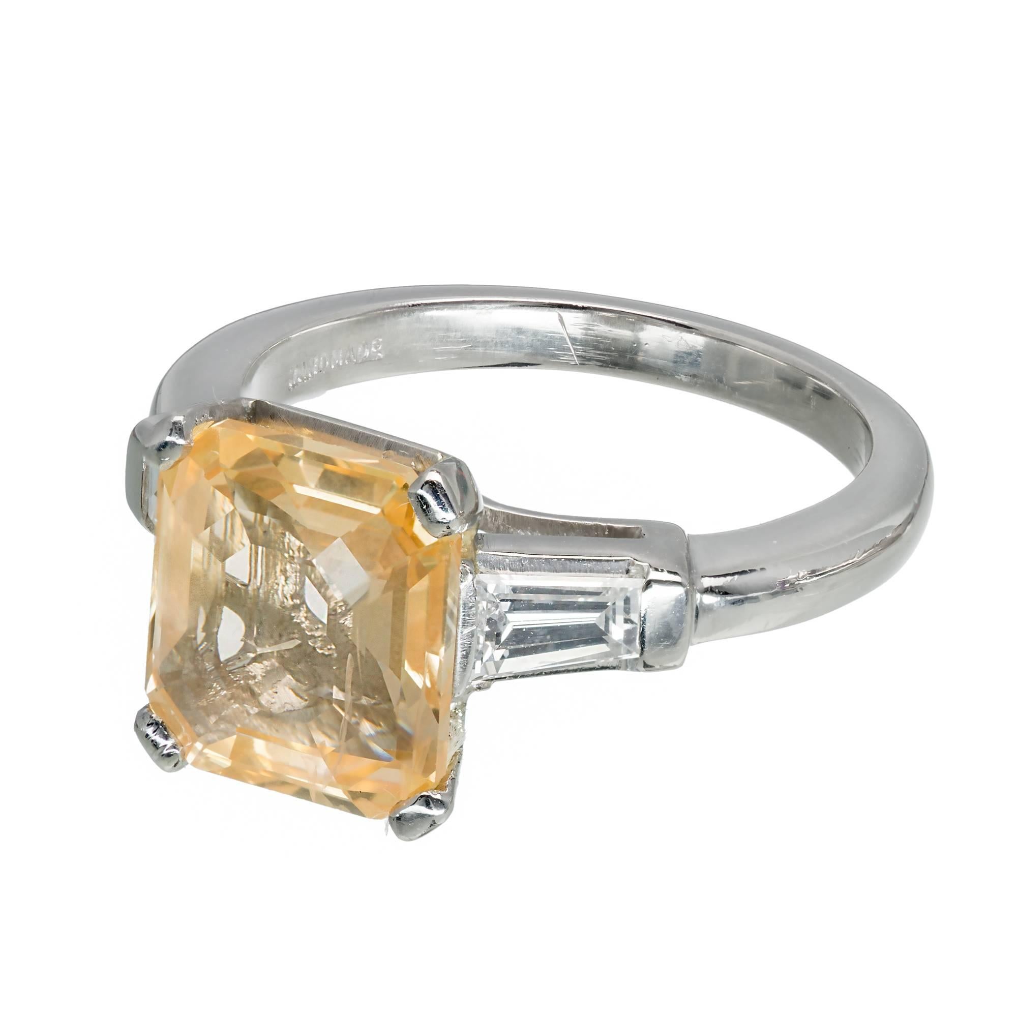 Three stone Natural orange yellow Emerald step cut Sapphire engagement ring. GIA certified in its original handmade Platinum setting with full size tapered baguette diamonds. Circa 1930-1940.

1 octagonal step cut orangey yellow Sapphire, approx.