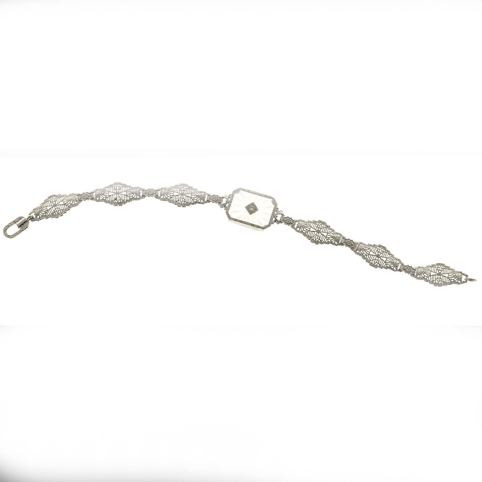 Pierced filigree link bracelet in 14k white gold. Original white gold hand engraved catch. The center piece is set with hand carved quartz crystal with one full cut diamond. Circa 1930.

1 round diamond approx. total weight .06cts
14k White