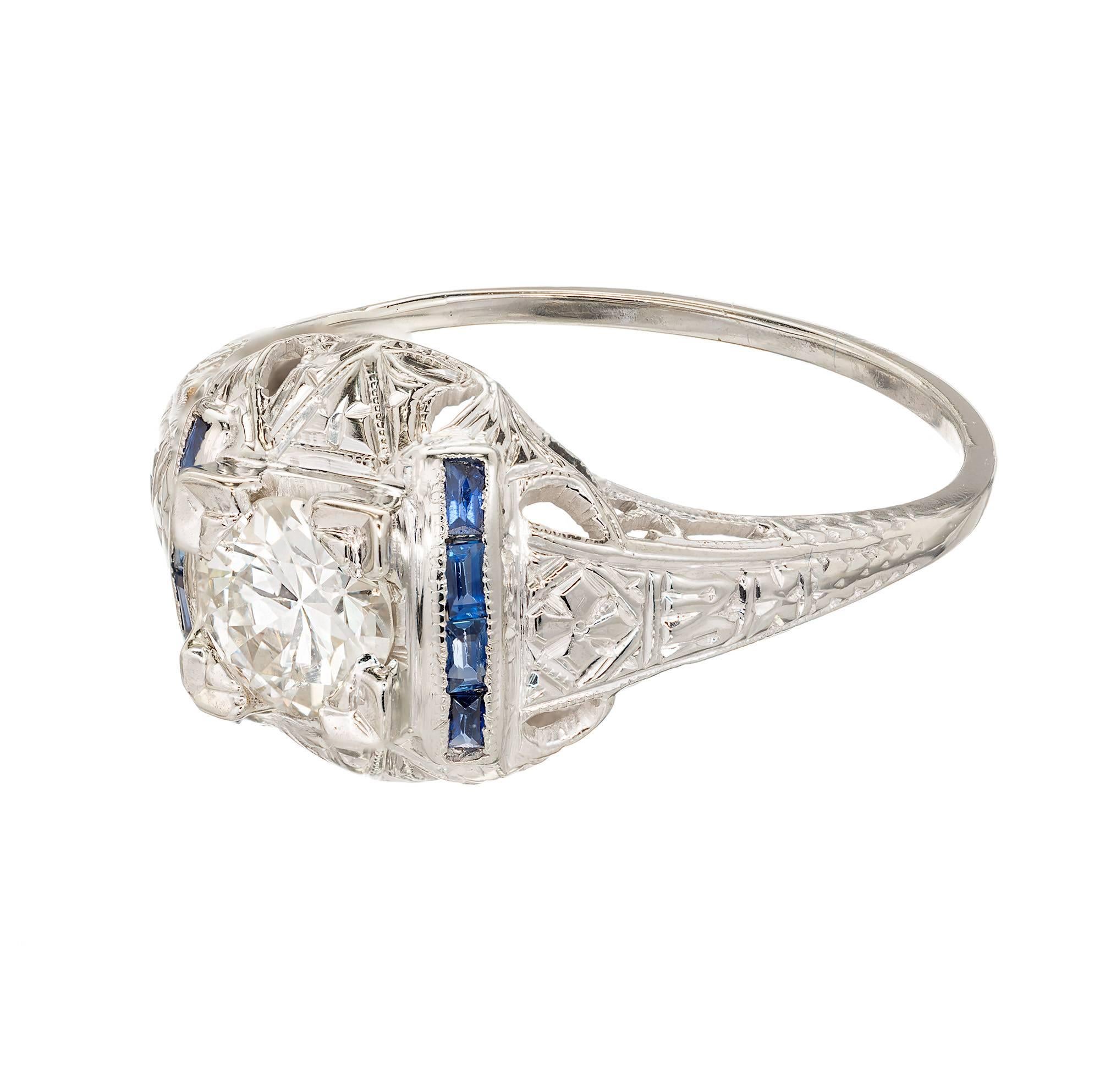 Handmade 1930s Art Deco filigree engagement ring. Domed top detailed with hand engraving. The center diamond is flanked by two rows of genuine calibre cut blue Sapphire baguettes.  The center diamond is a wonderful bright white transitional cut