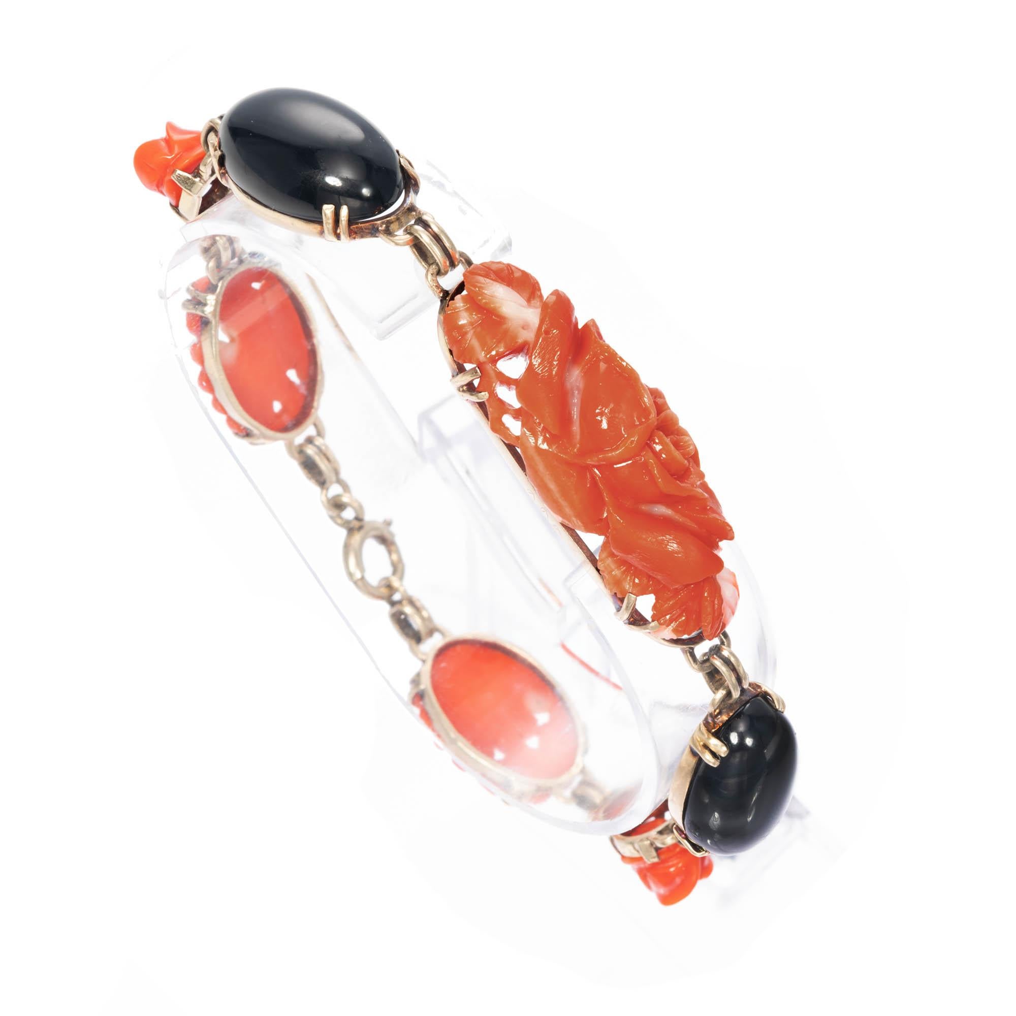 14k yellow gold natural coral and onyx bracelet. Rose carved natural mottled orange coral pieces set in 14k yellow gold with a large black onyx oval cabochon set on either side of center coral. The center coral piece is an elongated 3-Dimensional