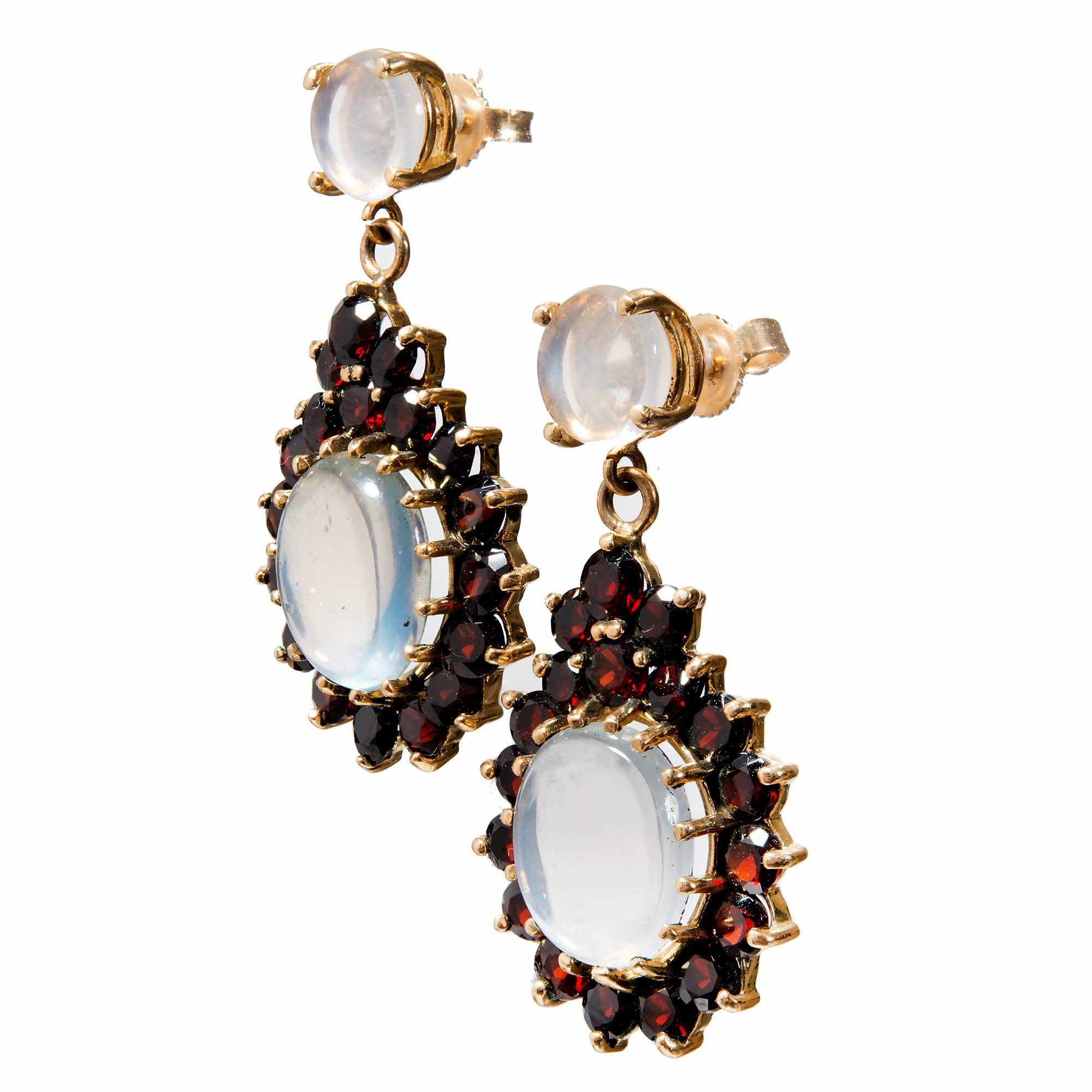 Moonstone and garnet dangle earrings. 2 round moonstone tops with 2 oval dangle moonstones with a halo of 36 round garnets in 14k yellow gold. 

2 blue round Moonstones 7.3mm
2 oval blue Moonstones (1) 11.5 x 10.5mm (1) 11.5 x 9.8mm
36 round Garnets