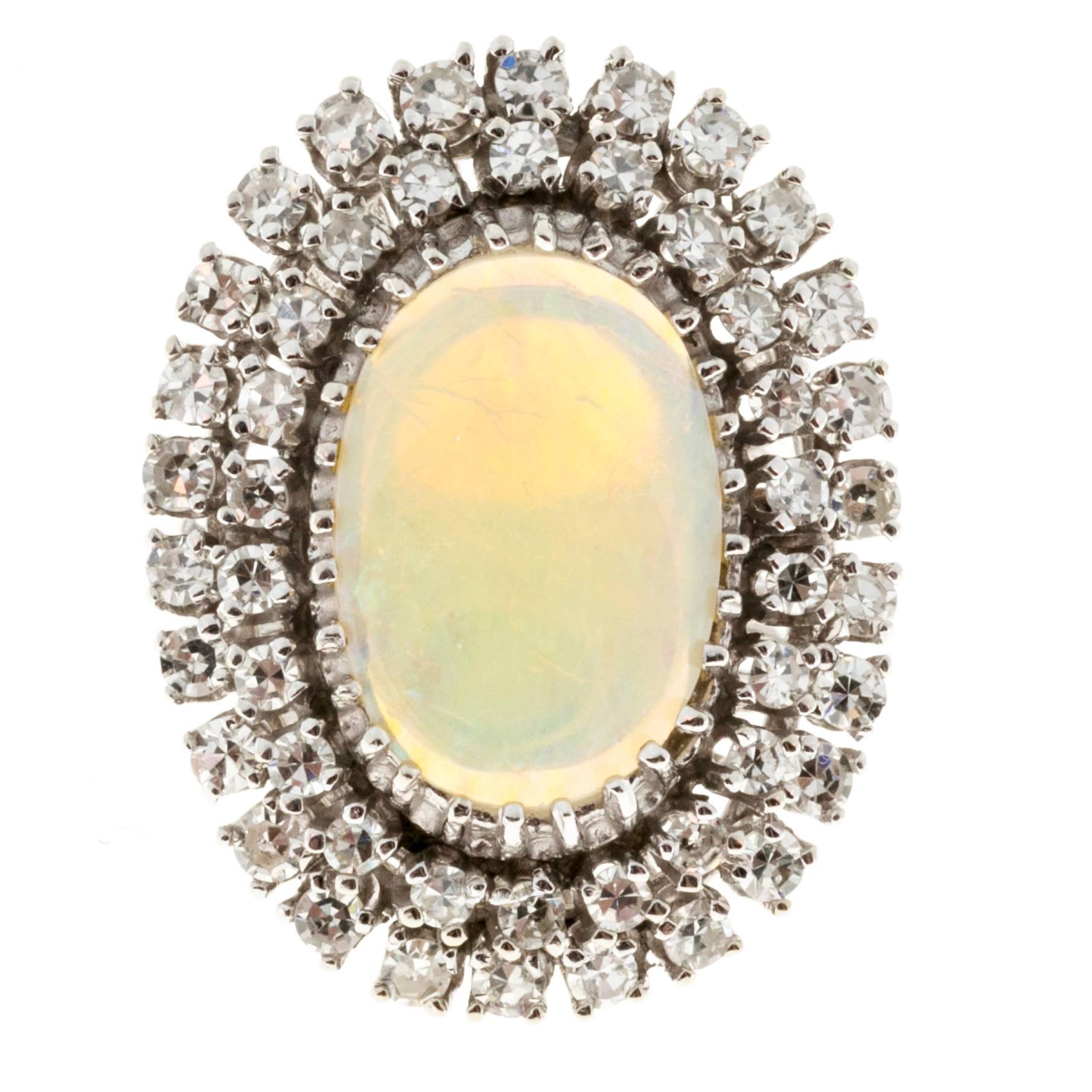 1960’s handmade wire construction crystal greenish blue clear opal with gentle swirls of color and hints of orange. The opal is surrounded by 2 rows of bright white single cut diamonds in a classic cocktail style.

1 oval opal 5/8 x 7/16 inch, 16