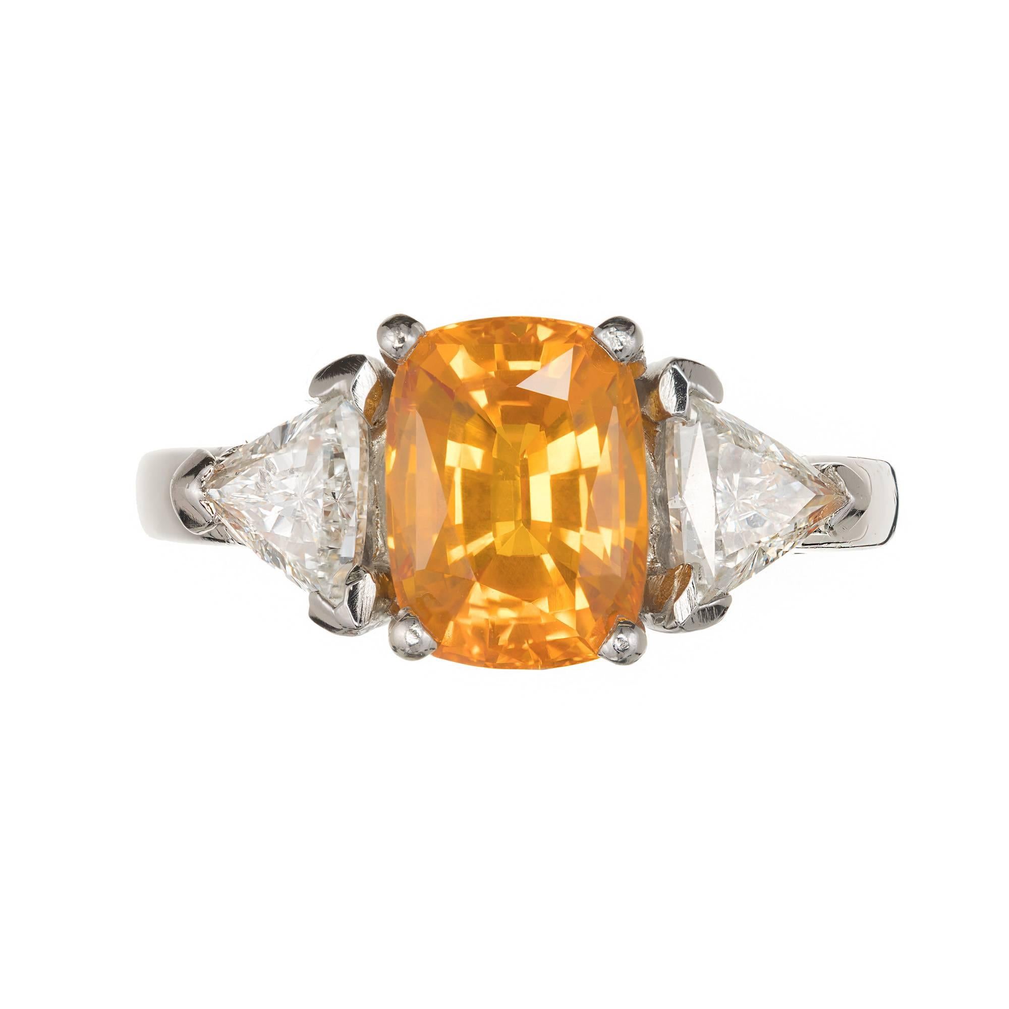 Cushion cut 2.89ct orange yellow Sapphire and trilliant cut diamond three-stone engagement ring. Simple low level heat only in a simple classic Platinum setting with two bright sparkly side diamonds.

1 cushion yellow Sapphire, approx. total weight