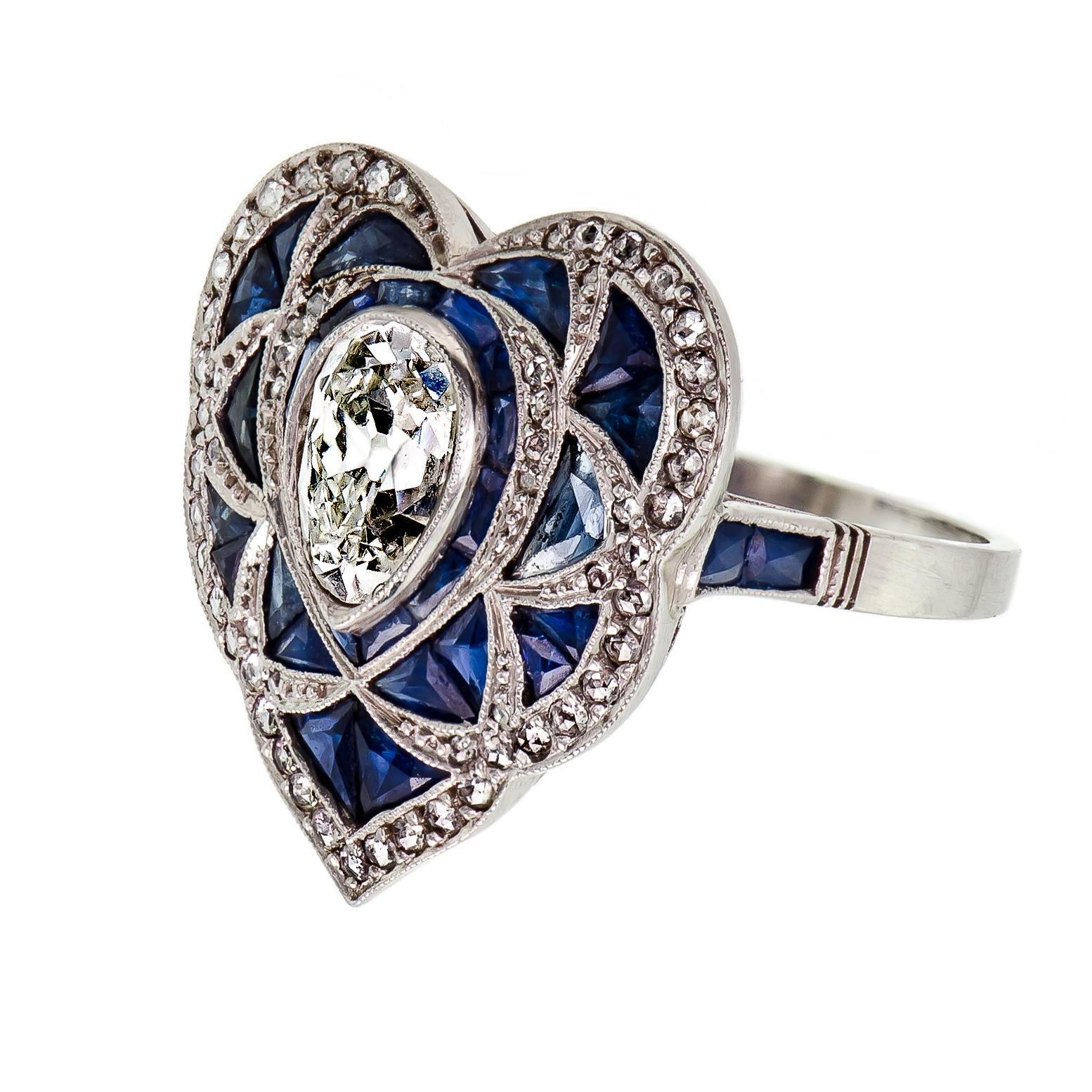 This large heart-shaped fabulous Art Deco diamond and sapphire ring handcrafted in a platinum mount. This ring contains one dazzling bezel set pear shaped cut diamond surrounded by enchanting baguette cut natural blue sapphires. This lovely ring has