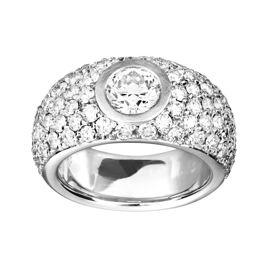 This striking diamond ring features a central 1 ct brilliant cut diamond, beautifully framed by 76 pave diamonds (0.03 ct each). The broad ring (size 53 / 6.5) is crafted in 18 karat white gold.