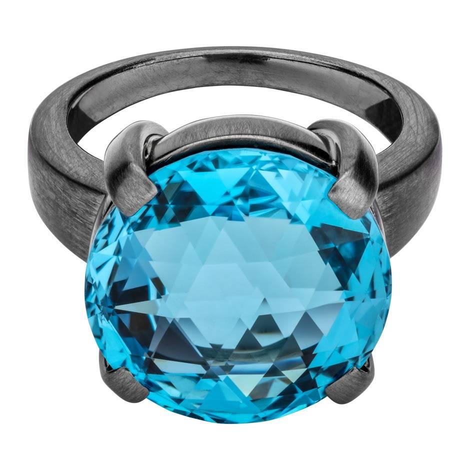 This modern cocktail ring features a facetted deep blue topaz (15 mm, 14.10 ct) in a classic prong setting. The ring is crafted in 18 karat matted rhodium plated white gold.