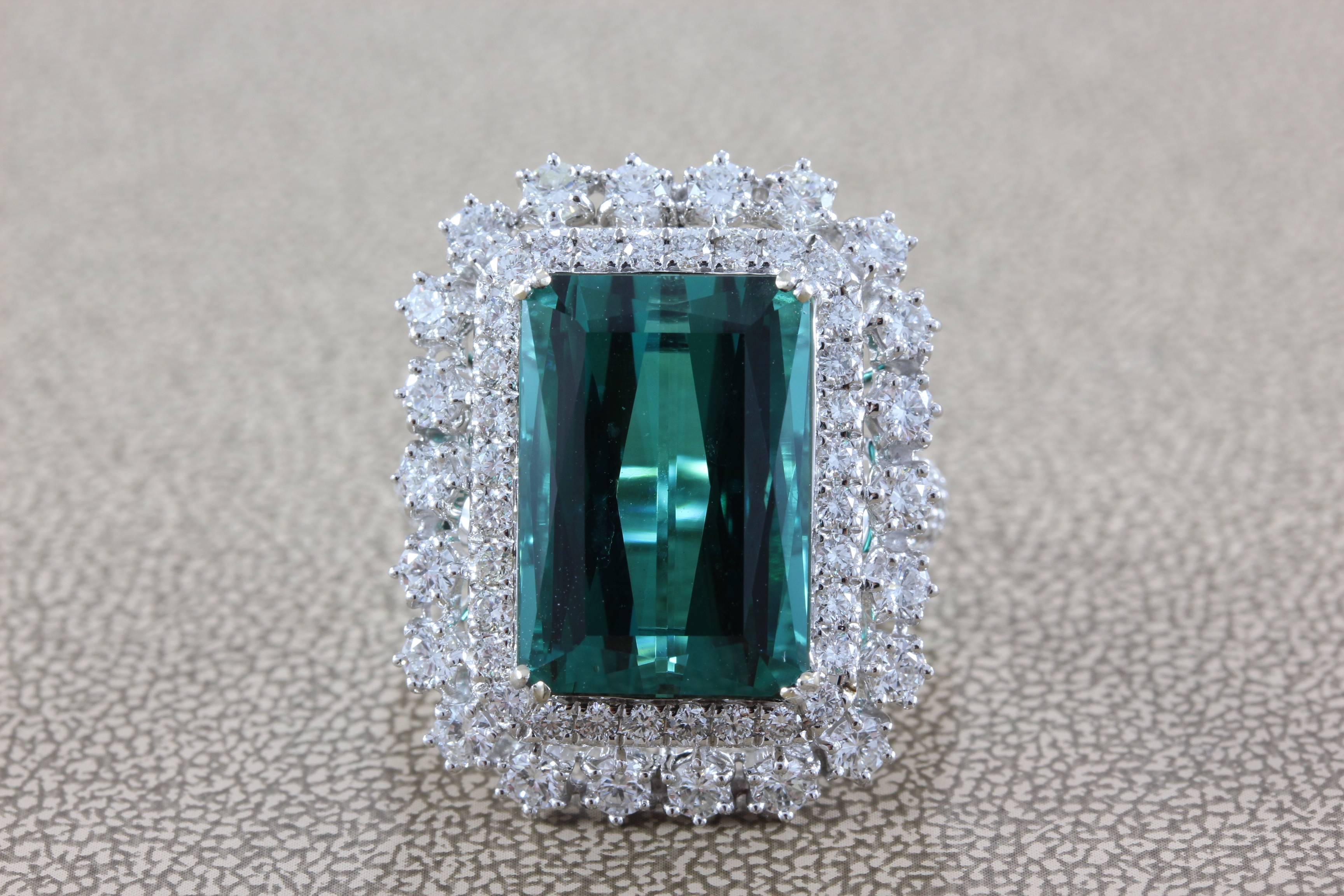 This royal ring features a 12.90 carat fancy cut Green Blue tourmaline which has been tested and certified by the GIA laboratory. The tourmaline features an even richly saturated color tone found in top gem quality tourmaline. A double halo of round