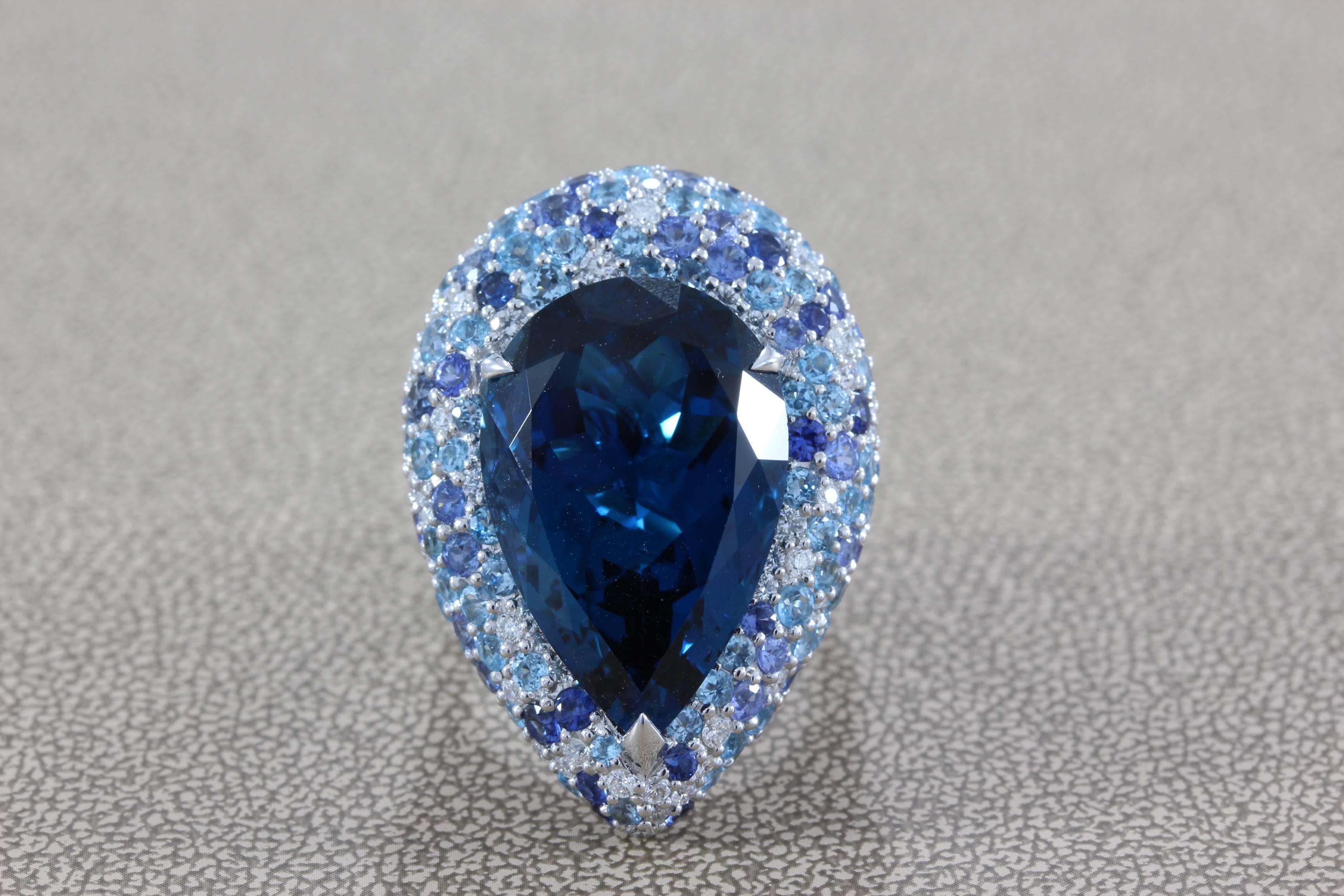 A large cocktail ring featuring a 25.76 carat pear shape blue topaz which is cut to perfection. Surrounding the center stone is a cluster of round cut diamonds and sapphires, set in 18K white gold, which total to 5.69 carats. A bold ring for a