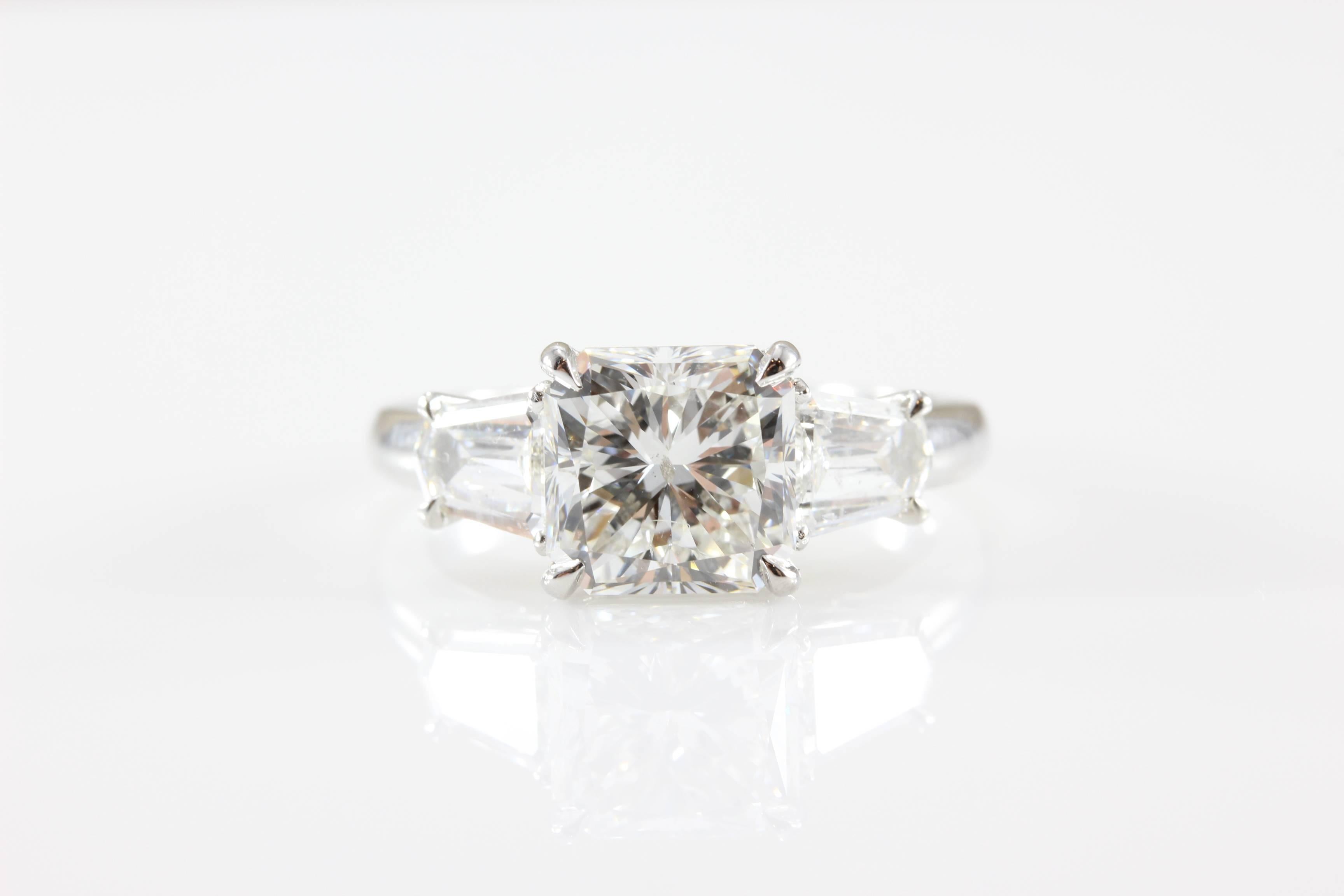 Ein spektakulärer Diamant mit 3,22 Karat im Brillantschliff ist modern mit zwei seitlichen Diamanten im Cadillac-Stil (1,80 Karat) gefasst.  Dieser Diamant mit Strahlenschliff ist durch seine geschliffenen Ecken noch einzigartiger.  Dieser Ring hat