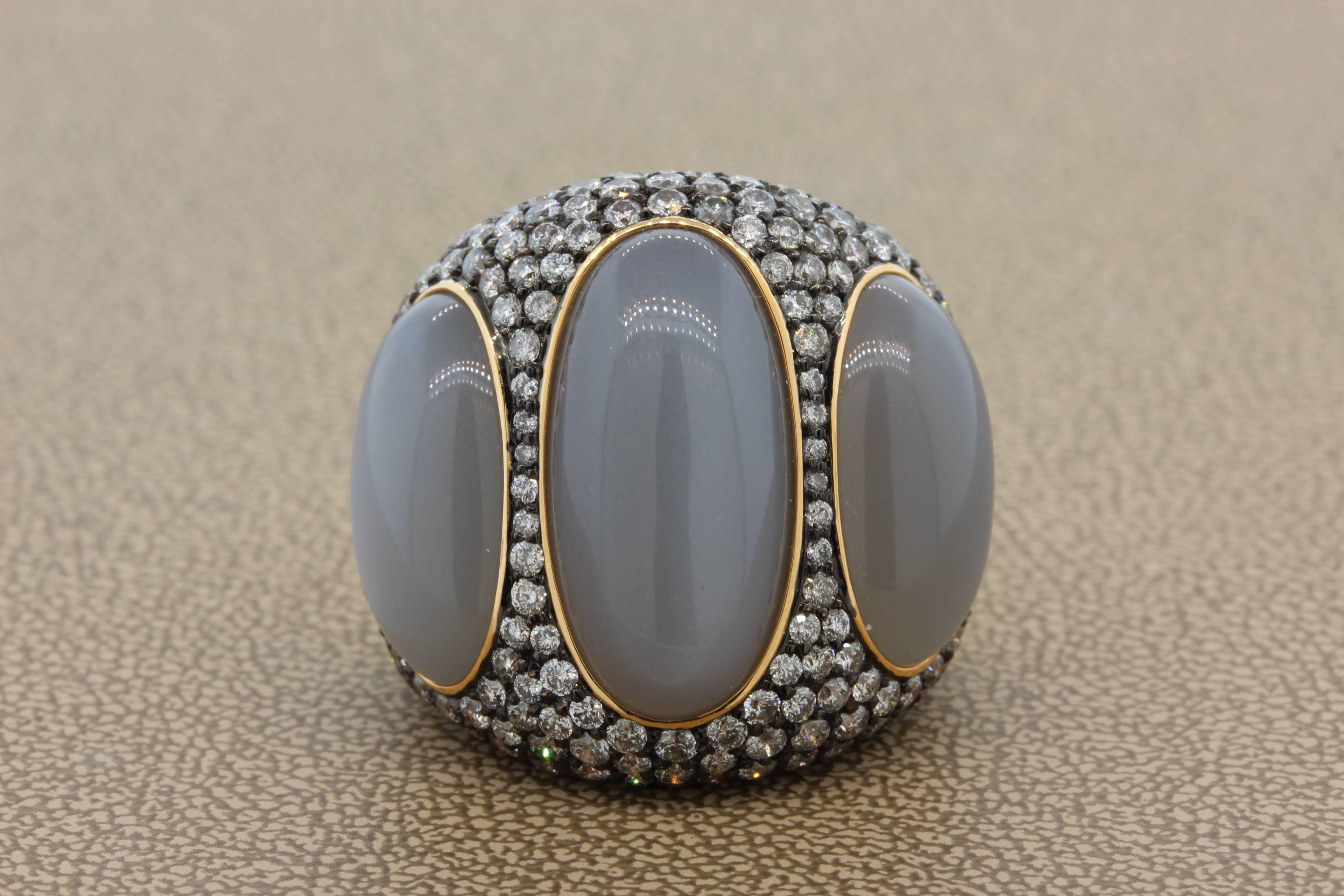 A lovely and unique cocktail ring fearing 3 pieces of luminous gray moonstone weighting 25.65 carats. The moonstone is accented by 5.39 carats of VS quality round cut diamonds which are set into 18K black rhodium gold. The rest of the ring is 18K