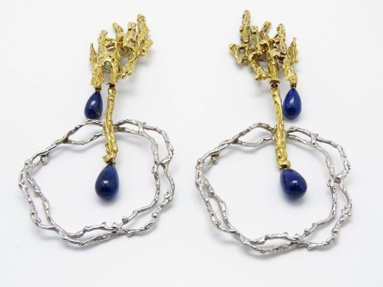 Earring clips that can be transformed.
Each asymmetrical face is composed of textured 18k yellow gold ending with a lapis lazuli drop and holding by a yellow gold segment a textured grey gold double ring.
The grey gold part can be detached.
It
