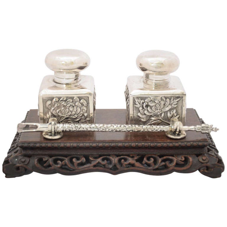 A Chinese Export Silver and wood Inkstand with dip-pen dating from around 1885. The hinged ink bottles are decorated with embossed chrysanthemum to the sides and the covers are plain. The pen has a figural end and it is a perfect size to complement