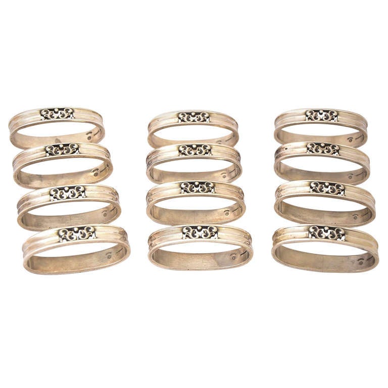 A set of 12 sterling silver napkin rings made by the firm of Georg Jensen and designed by Johan Rohde. These 12 oval, scroll-pattern rings were made in Copenhagen post 1945.