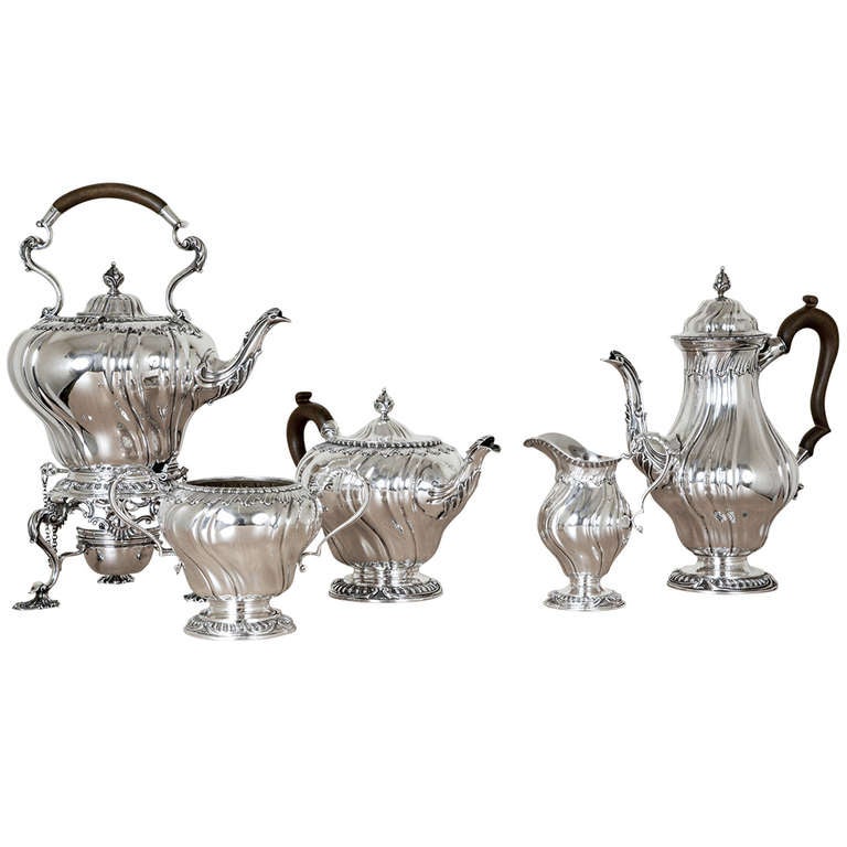 A Sterling Silver Tea & Coffee Service comprising of a coffee pot, teapot, kettle on stand with lamp, sugar basin and cream jug. It is of spiral flute design with gadroon borders and acanthus leaf spouts, and is dated London 1903-19. The maker is