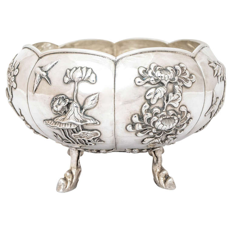 A Chinese Export Silver Bowl marked KMS for Kwong Man Shing, who was making and selling in Hong Kong in the late 19th and early 20th Century. The eight panels are applied with foliage and birds and the bowl stands on 4 legs modelled as