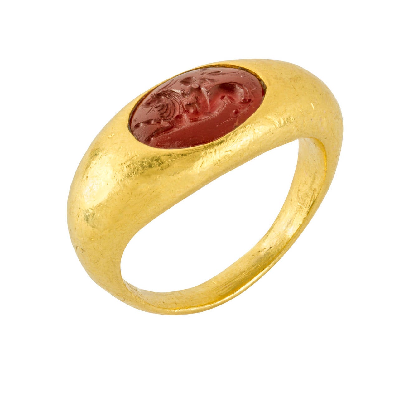 A Roman hardstone intaglio ring, the carnelian intaglio finely carved with a winged figure of Cupid holding a beribboned staff, riding a mythical creature with the head of a lion and the body of a goat, rubover set within a yellow gold elliptical