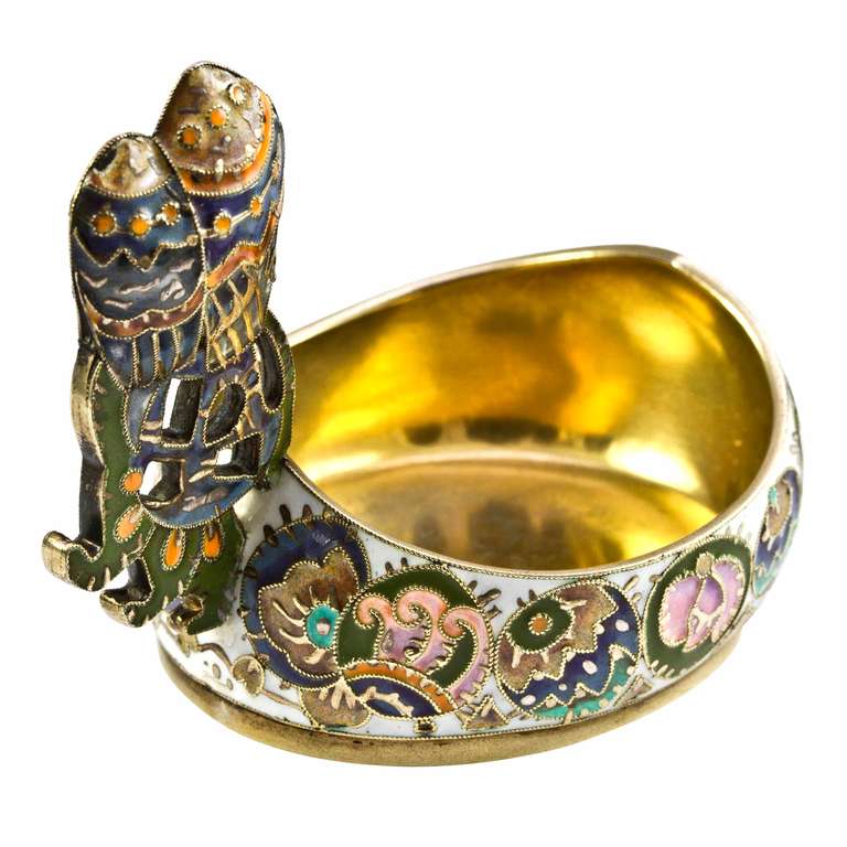 A Fabergé silver-gilt and cloisonné enamel kovsh, the body of traditional form decorated in the pan-slavic style with varicoloured geometric designs on a white enamel background, the raised handle in the form of stylised owls sitting on a perch of
