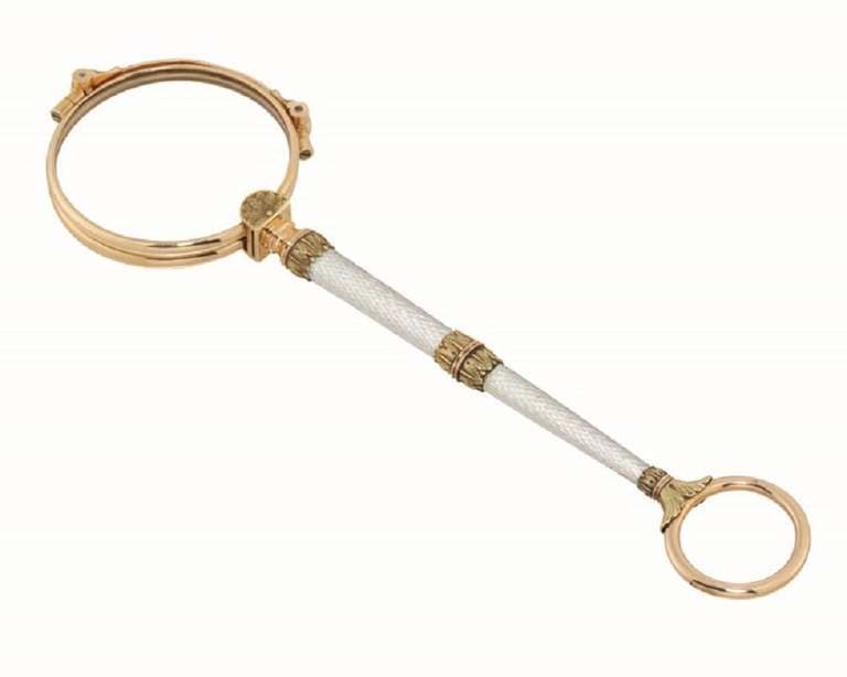An important Fabergé enamel and gold lorgnette, the lorgnette comprising two circular lens within a rose gold mount, with exquisite pearl white enamel handle with engine-turned background, with yellow and rose gold floral decoration and ring