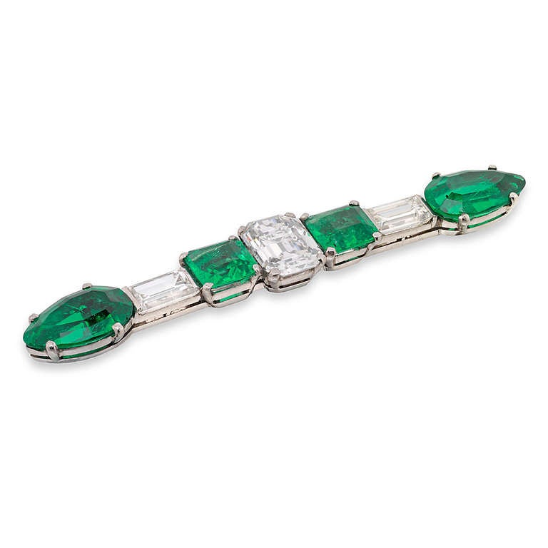 An Art Deco emerald and diamond bar brooch, the brooch set with a central emerald-cut diamond weighing 1.35 carats, of E colour SI1 clarity, two square step-cut emeralds to either side weighing a total of 1.28 carats, an emerald-cut diamond to