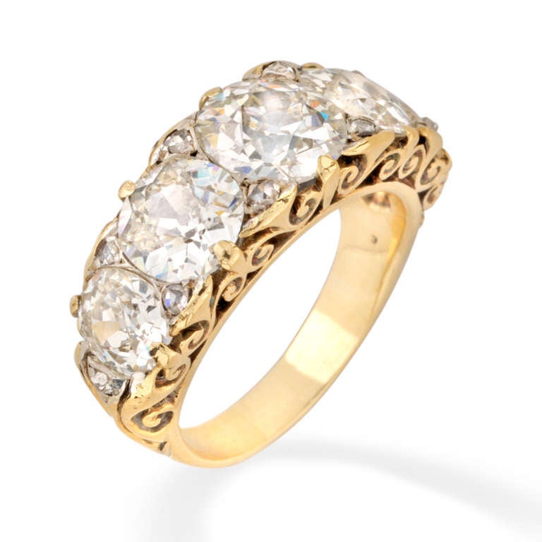 A Victorian half carved hoop five stone diamond ring, the five graduating old brilliant-cut diamonds weighing a total of 5.45 carats all set in gold to a scrolled pierced gallery embellished with rose-cut diamonds, circa 1880.