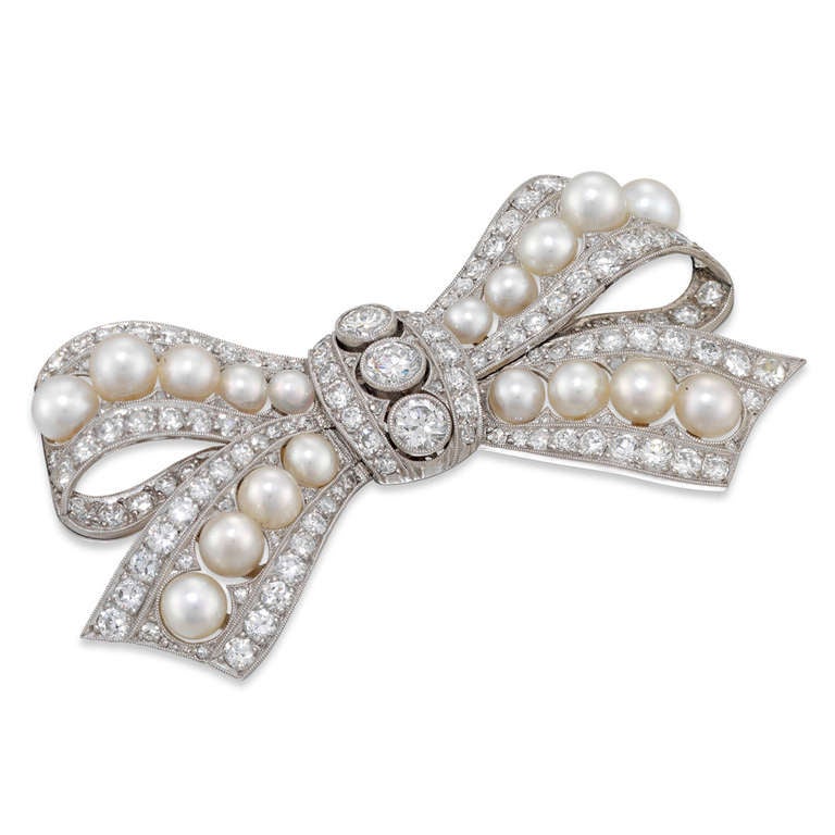 A fine Edwardian natural pearl and diamond bow brooch, the pierced ribbon tied bow encrusted with old brilliant-cut diamonds, estimated to weigh a total of 4.4 carats, with a central run of graduated natural pearls, with certificate from the