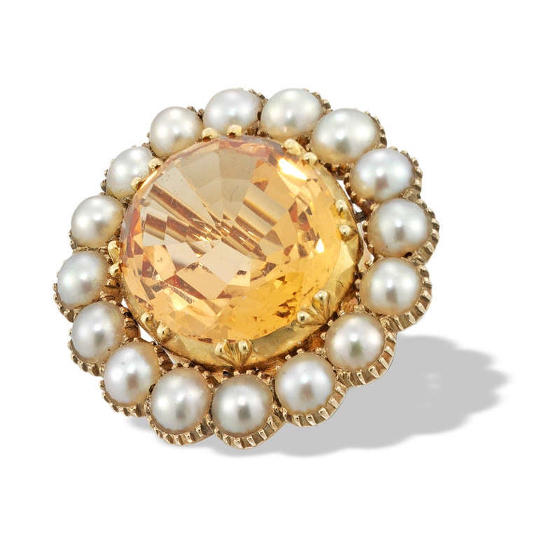 A Georgian topaz and pearl cluster brooch, the oval faceted topaz estimated to weigh 5.20 carats in a cut-down setting, surrounded by a half pearl cluster all to a yellow gold mount, with brooch fitting, circa 1800, measuring approximately 2 x