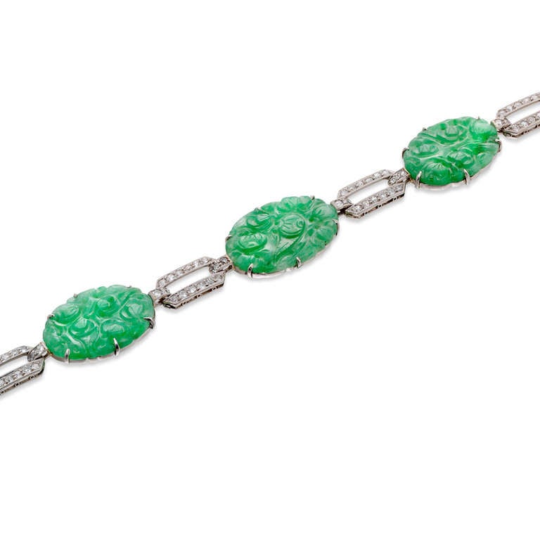 An Art Deco jade and diamond bracelet, the bracelet comprising five ornately carved oval jade plaques, measuring approximately 20.6 x 14.7 mm, a diamond-set geometric openwork link in between each, estimated to weigh a total of 1.60 carats, all set