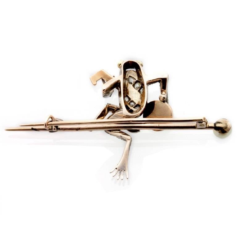 A Victorian diamond set frog novelty bar brooch, the old and rose-cut diamond frog seated on a bar terminated in a pearl and playing a golden banjo, the diamonds silver-set and mounted on gold, circa 1880.