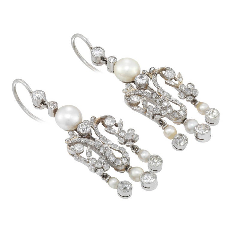 A pair of late Victorian pearl and diamond drop earrings, the earrings comprising a natural pearl surmount with two diamonds above, the pearl measuring approximately 6.5mm in diameter, surmounting a rose-cut and old-cut diamond-set fringe of floral