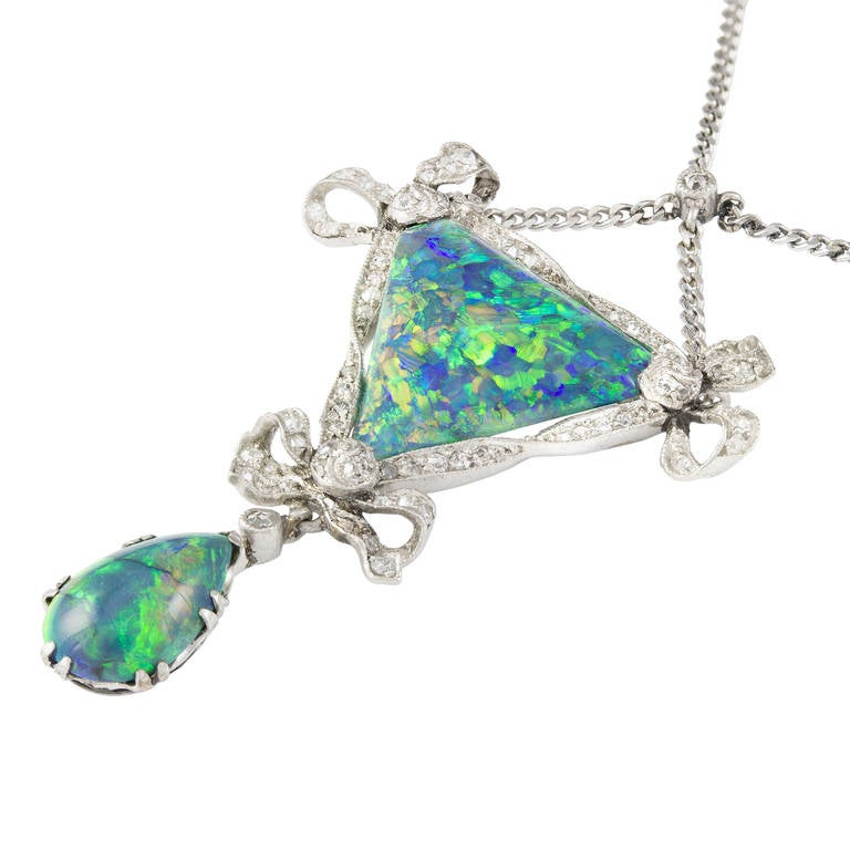 An Edwardian opal and diamond pendant, the triangular-shaped black opal set within a single-cut and rose diamond-set border of twisted ribbon and bow design with a pear-shaped black opal drop beneath, all set to a platinum mount suspended from a