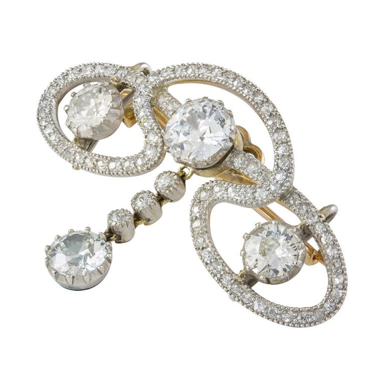 Spilla a voluta di diamanti in stile Art Nouveau. La spilla comprende tre diamanti taglio brillante antico, all'interno di una voluta traforata con diamanti incastonati, con una goccia di diamante taglio brillante antico al centro; i diamanti hanno