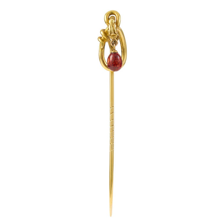 A Fabergé yellow gold stick pin with coiled snake motif surmount, the serpent's mouth suspending a miniature egg in translucent raspberry red enamel with guilloché ground, Workmaster E Schramm, St Petersburg, late nineteenth century, dimensions