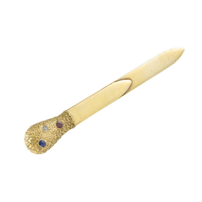 A Fabergé yellow gold and gem-set paperknife with book-blade, with a "samaradok" molten texture handle set with a ruby, sapphire and diamond, workmaster Eric Kollin, St Petersburg, measuring 12.5cm x 1.5cm, circa 1890, gross weight 24.6