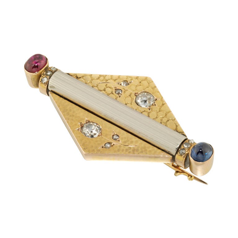 A Faberge ruby, sapphire and diamond lozenge-shaped brooch, with a white fluted baton-shaped motif set with a cabochon-cut sapphire and ruby at finials, with rose-cut diamond collars, on a yellow gold lozenge shaped plaque with two different