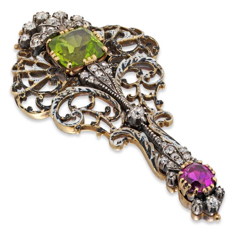An enamel and gem-set brooch by Giuliano, the stylized feather-shaped brooch of pierced scroll-work decorated with black and white enamel, claw set with a cushion shaped peridot measuring approximately 9 x 8mm, and a similarly cut and set ruby