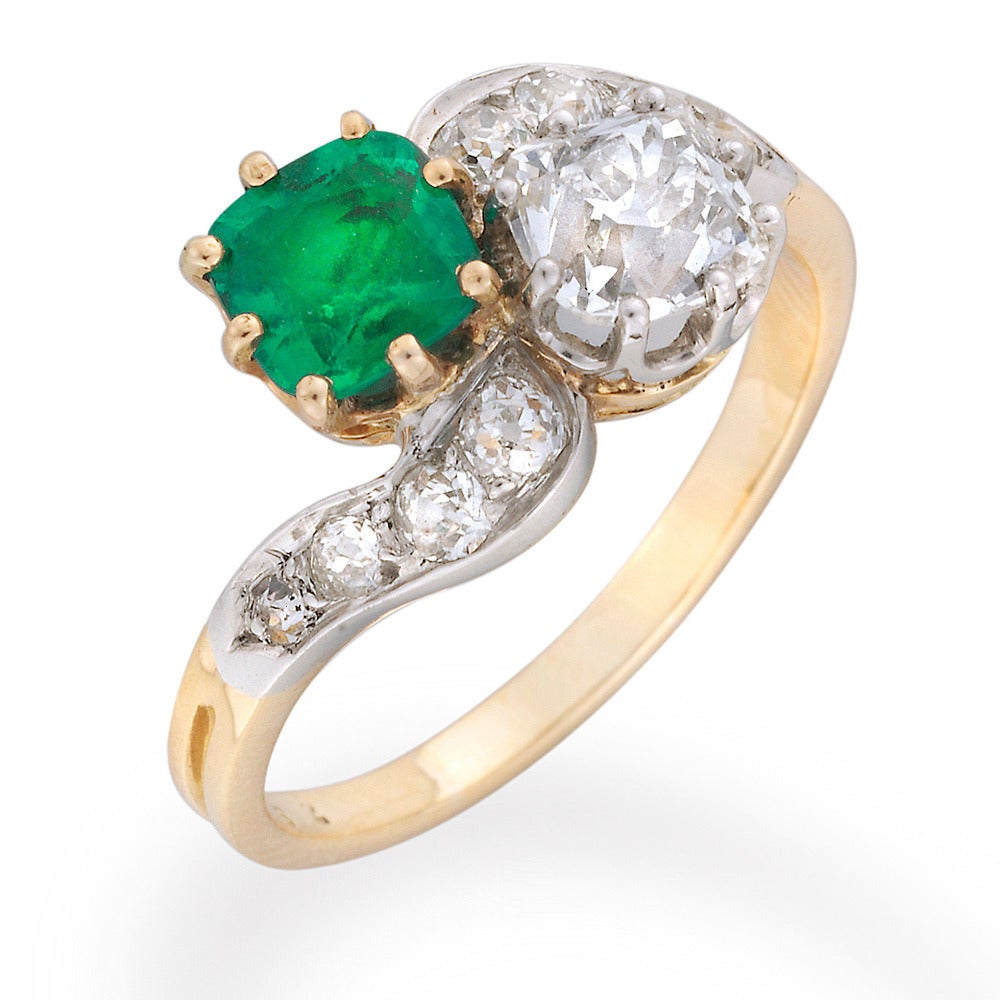 An Edwardian emerald and diamond crossover ring, the ring set with a cushion-cut emerald weighing 0.73 carats, claw-set in yellow gold, and a cushion-cut diamond weighing 0.95 carats, claw-set in platinum to a yellow gold mount, four graudated