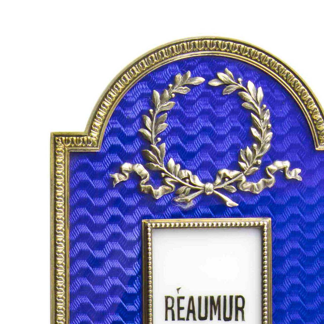An Imperial Fabergé silver-gilt and enamel thermometer, of rectangular form with semi-circular ends, the surface enamelled in translucent royal blue over banded wavy engine-turning within a leaf tip border, the bead-framed aperture enclosing a white