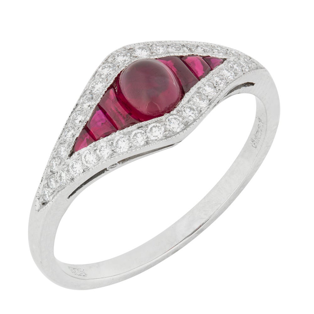 A ruby and diamond cluster ring, the ring comprised of a central oval-shaped cabochon-cut ruby, with calibre-cut rubies set to either side, estimated to weigh a total of 0.65 carats, set within an elongated diamond-shaped diamond-set cluster