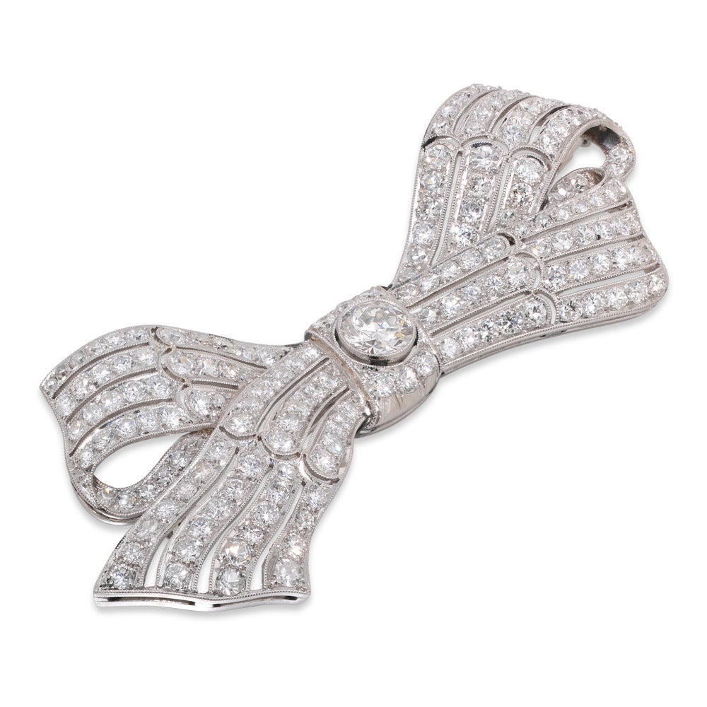 A fine diamond-set bow brooch, the pierced tied ribbon bow encrusted throughout with round brilliant-cut diamonds, weighing approximately 5 ½ carats in total, the knot set to the centre with a larger round brilliant-cut diamond, weighing