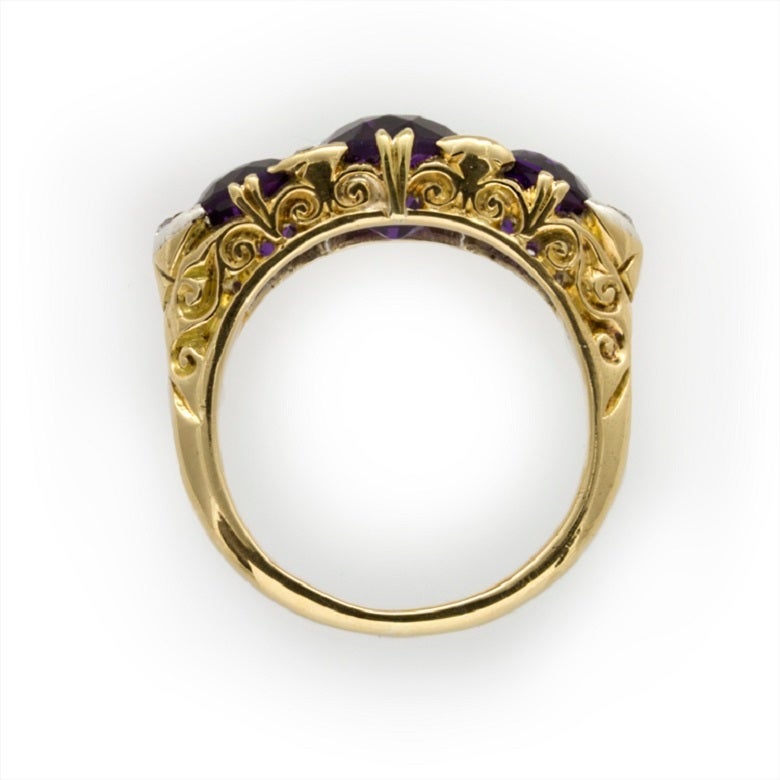 A Victorian amethyst three stone ring, the three claw-set round faceted amethysts weighing approximately 3.5 carats in total with six small old-cut diamonds weighing an estimate total of 0.2 carats inbetween, all to an 18 carat yellow gold ornately