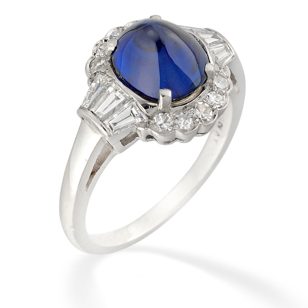A sapphire and diamond cluster ring, the sugarloaf cabochon-cut sapphire estimated to weigh 3.3 carats, set to the centre of a cluster surround of ten eight-cut diamonds, with three tapered baguette-cut diamonds to each shoulder, the diamonds