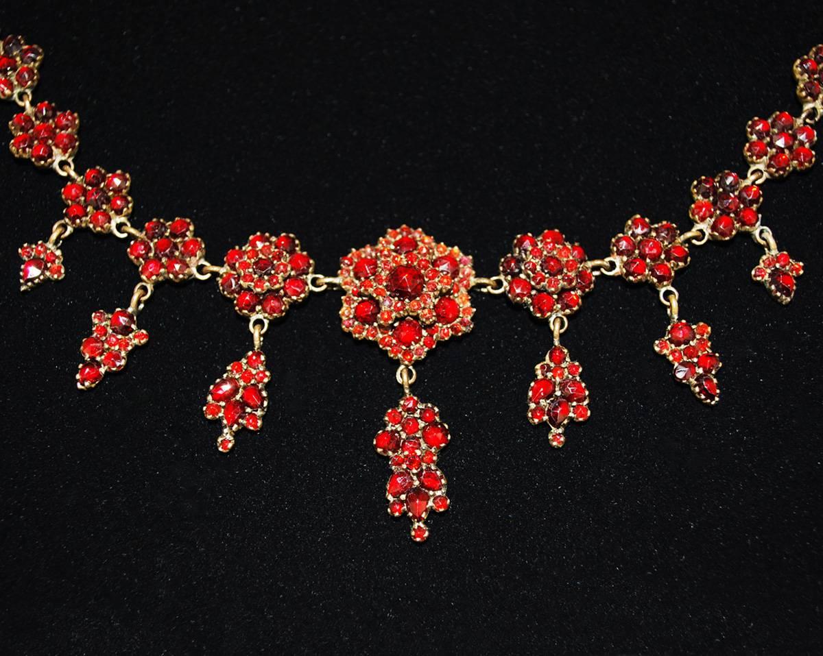 A stunning set of antique Bohemian garnet jewelry, each piece brimming with the copious bright red stones. The necklace features 30 links, each displays a stylized floral shape. The central seven links get larger towards the middle and have elegant,