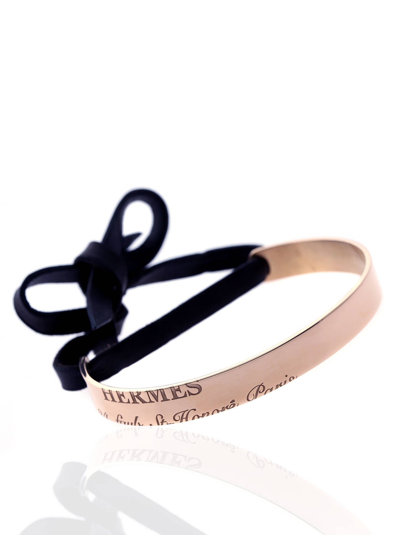 A chic authentic Hermes cuff featuring engravings of the brand maker and address in Paris in 18k rose gold, to seal the deal a contrasting black leather has been added which can be tied.

Length: 16cm (6.28" Inches)
Dimensions: .31″ Inches