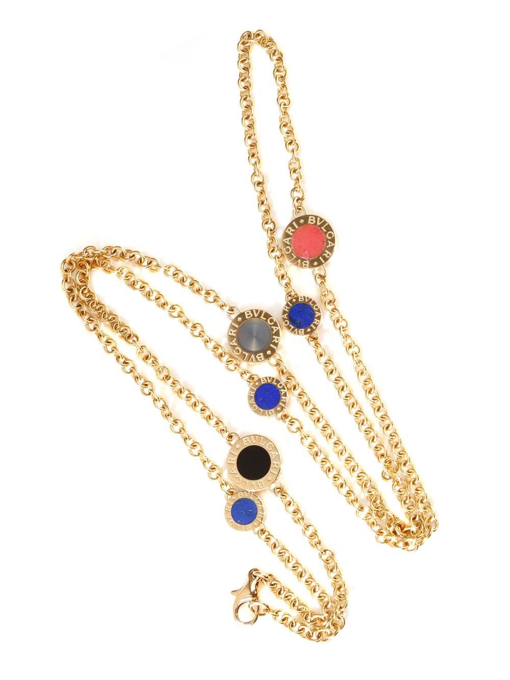 Yellow gold links and precious stones form this daring necklace. Meticulously crafted links are the accessory’s base while the designer’s name is a prominent feature. Enhancing the piece are onyx, coral and lapis. These stones are displayed within a
