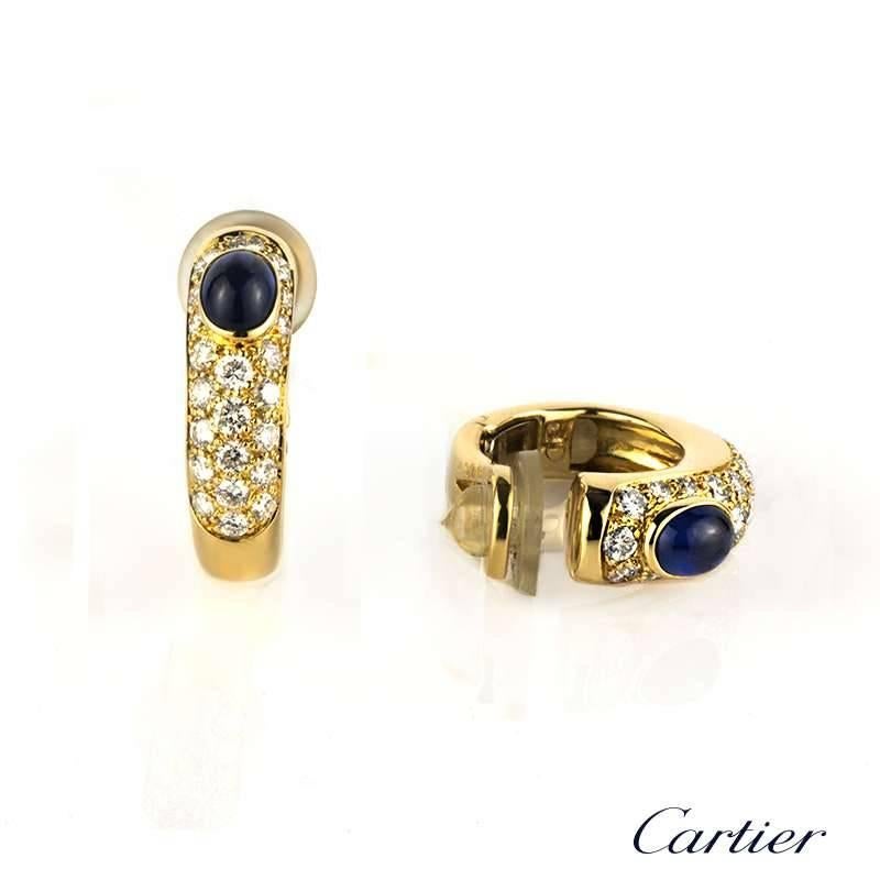A pair of 18k yellow gold diamond and sapphire set earrings by Cartier. The earrings are set to the centre with a 0.40ct rubover set cabochon cut sapphire complemented by 22 pave set graduating round brilliant cut diamonds totalling approximately