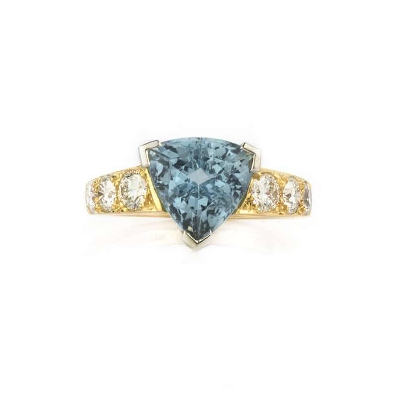 A 22k yellow gold aquamarine and diamond ring. The ring comprises of a trilliant cut aquamarine centre stone set in a three claw setting, weighing approximately 3.20ct, dispersing an intense blue hue throughout. Accentuating the central stone are 6