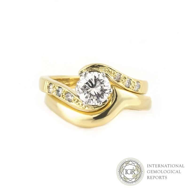 A unique twist design 18k yellow gold diamond ring with a matching band. The round brilliant cut diamond weighs 0.71ct, is G colour and SI1 clarity, set between a twist design diamond set mount. Either side of the diamond is set with three round